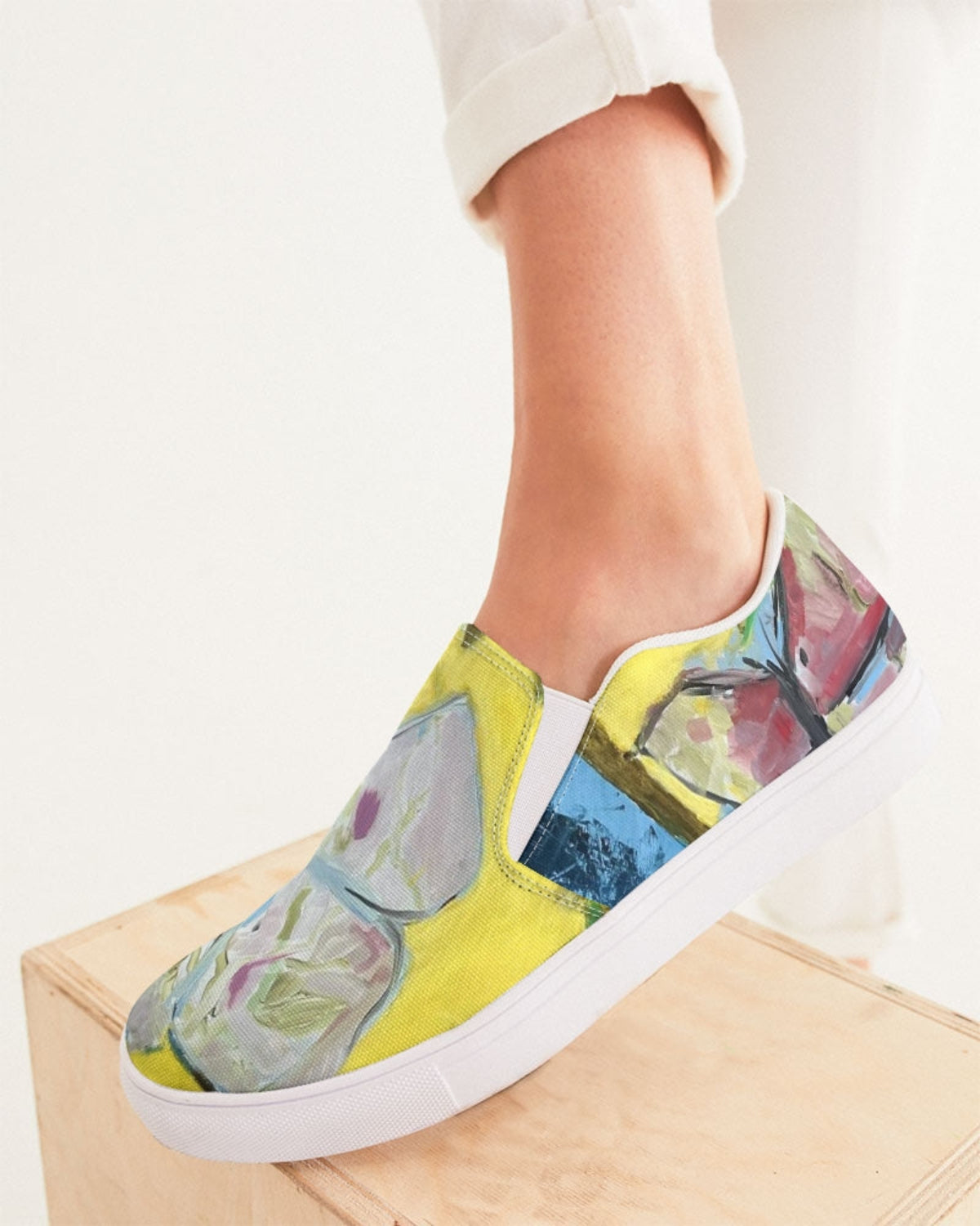 Colorful slip-on sneakers with abstract design worn by a person on a white background