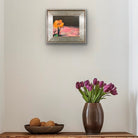 Framed artwork above a wooden console table with a vase of purple tulips and decorative items.