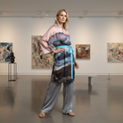 Woman in a stylish outfit standing in an art gallery with abstract paintings on the wall.