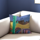 Decorative pillow with a colorful landscape design on a white couch against a blue wall.