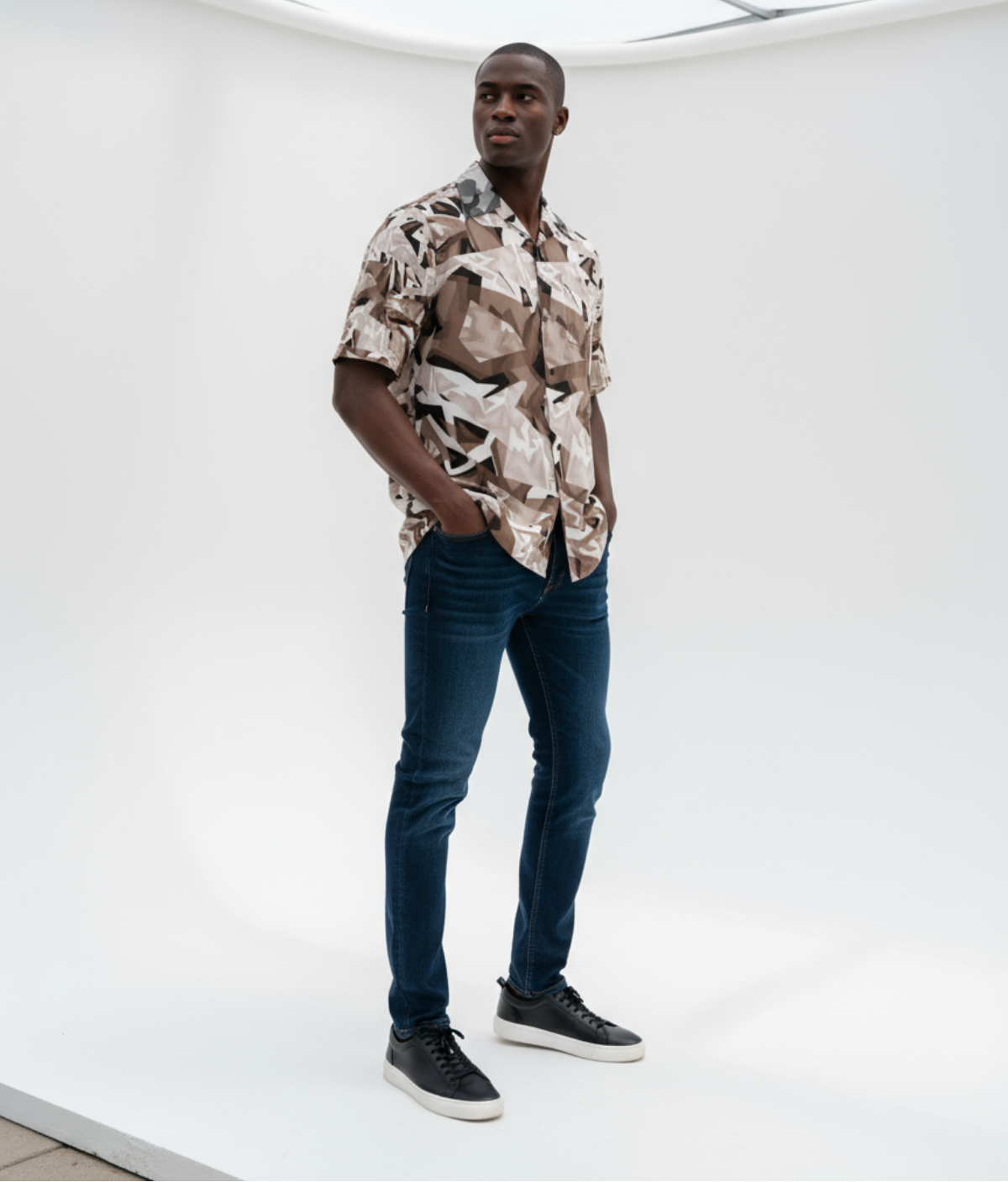 Black fashion model wearing a patterned shirt and jeans standing in a minimal studio