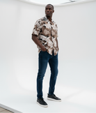 Black fashion model wearing a patterned shirt and jeans standing in a minimal studio