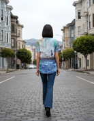 Woman walking down a street wearing a colorful shirt with a scenic print