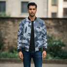 Man wearing a blue camouflage bomber jacket and dark jeans standing outdoors.