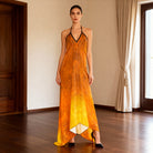 Woman wearing an orange and yellow dress in a room with wooden floor and white walls.