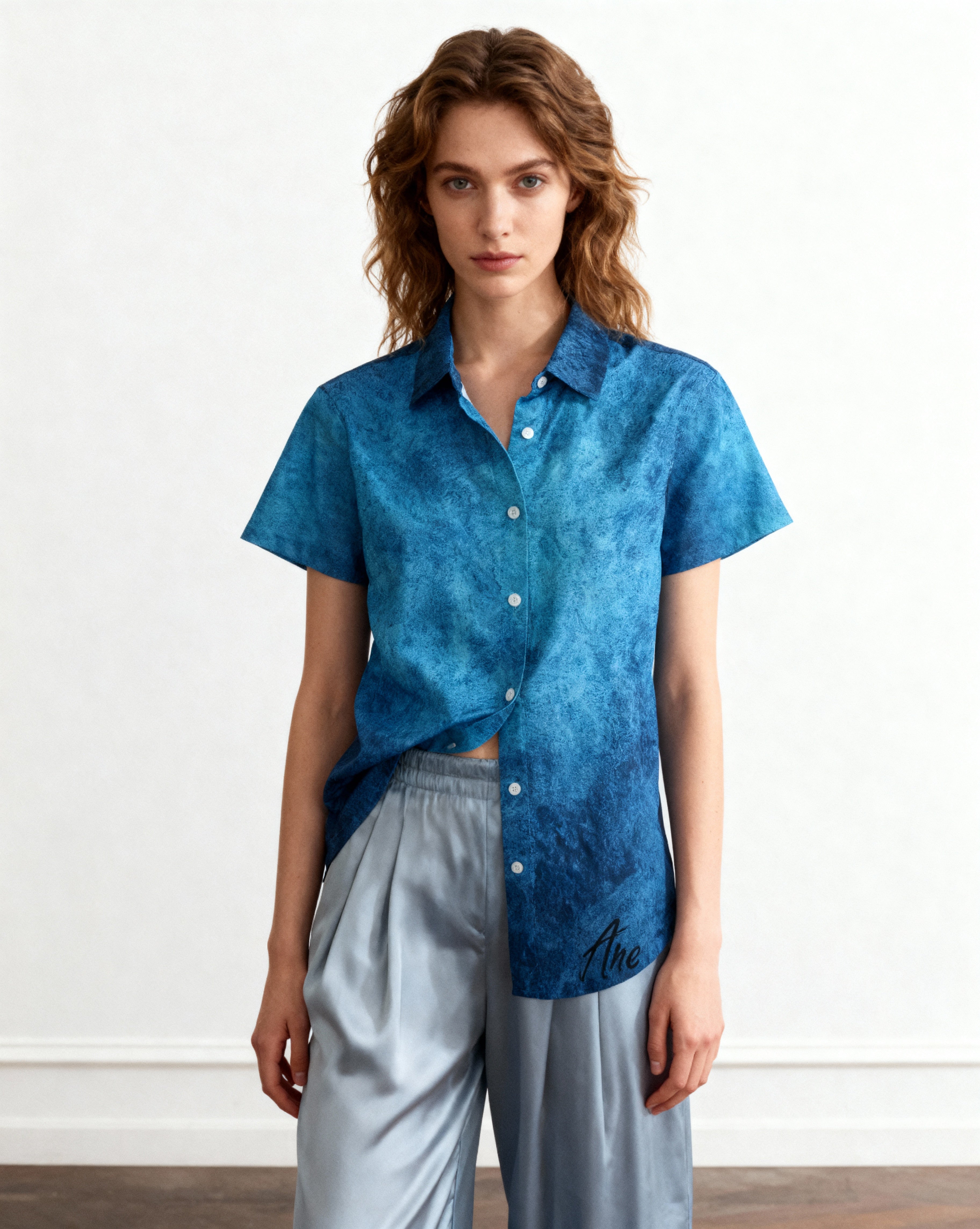 Woman wearing a blue patterned shirt and light gray pants against a white background