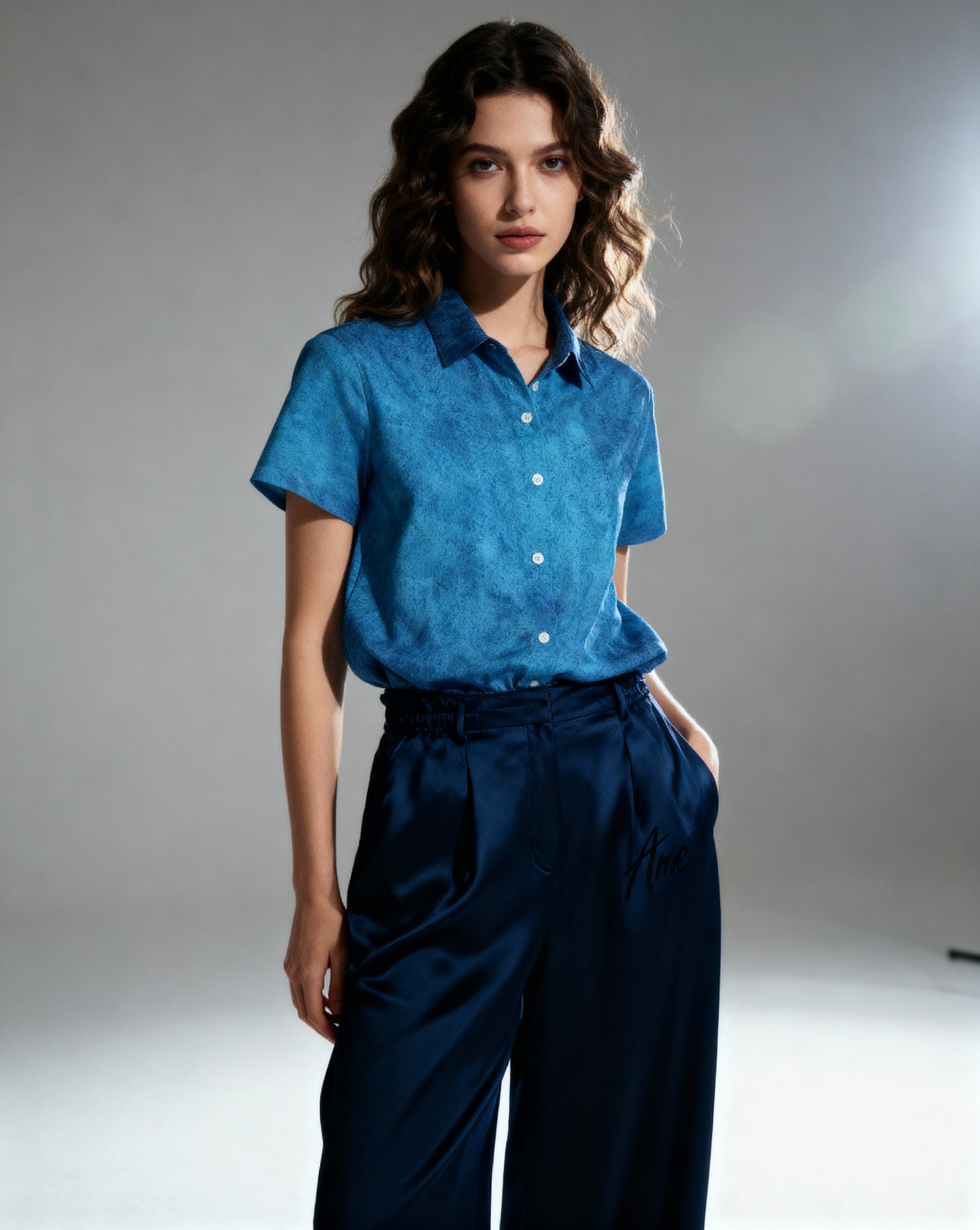 Woman wearing a blue shirt and navy pants against a gray background